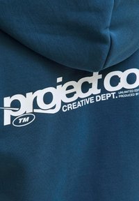 Felpa blu realizzata in tessuto morbido, con un grande logo bianco recante la scritta "project co" e il testo "CREATIVE DEPT." sul retro.