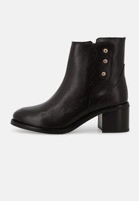 Stivaletto alla caviglia in pelle nera con punta arrotondata, tacco medio a blocco e bottoni decorativi in tonalità oro sul lato, con dettagli cuciti.