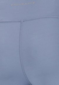 Ljusblå idrottsshorts tillverkade av ett smidigt, elastiskt material. Har flatlock-sömmar och ordet "ENDURANCE" tryckt i guld.