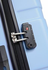 Hard-shell suitcase in light blue with a textured finish, featuring a black TSA-approved lock, silver zipper hardware, and black trim.