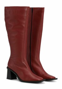 Térd fölé érő piros bőrcipők hegyes orral, tömbsarkal és oldalsó cipzárral. Sima textúrájú, karcsú, illeszkedő kialakítással.