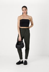 Haut noir sans bretelles avec texture froncée, pantalons olive ajustés avec ceinture à nouer, sac à main noir et chaussures noires épaisses.