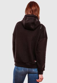Sudadera negra con una gran capucha, mangas largas y puños acanalados. Presenta detalles con cremallera en los hombros y una etiqueta de la marca roja en el dobladillo.