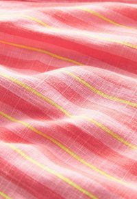 Tissu textile rose pâle avec une surface texturée et des rayures horizontales jaunes. Le tissu semble doux et légèrement froissé.