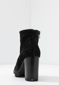Bottines en suede noir avec un talon épais et haut, et une fermeture éclair à l'arrière. Tissu texturé avec une finition lisse sur le talon.