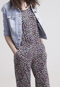 Mono de estampado de leopardo con cintura elástica y bolsillos, combinado con una chaqueta de mezclilla azul claro de manga corta y botones plateados.