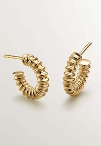 Pendientes de aro en tono dorado con un diseño texturizado y ondulado, que cuentan con un cierre circular liso y un vástago estrechado para un ajuste seguro.