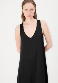 Svart ärmlös klänning med djup V-halsringning, tillverkad av mjukt tyg, med en avslappnad siluett och minimalistisk design.