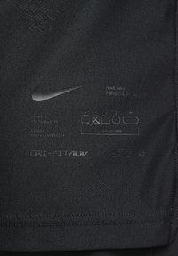 Mustan Nike-kankaan, jossa on näyttäv�ä logo, tekstiä, hoito-ohjeita sekä tietoja suorituskyvystä ja istuvuudesta. Sileäpintainen rakenne, jossa on selkeät yksityiskohdat.