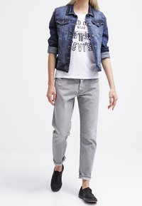 Jeansjacka i mörkblått, vit grafisk T-shirt, ljusgrå löst sittande jeans och svarta sneakers. Har uppvikt ärm och avslappnad design.