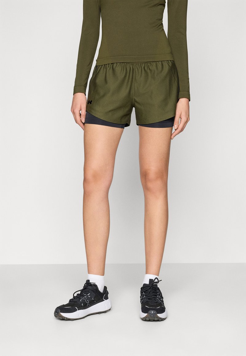 Olivengrønne sportsshorts med elastisk talje, lagd over sorte indershorts, parret med sorte og hvide løbesko.