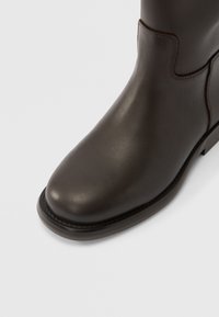 Καφέ δερμάτινο μποτάκι μέχρι τον αστράγαλο με λείο φινίρισμα, στρογγυλεμένη μύτη και διακριτικές ραφές. Ξεχωριστό σχέδιο στην πλαϊνή ραφή και ανθεκτική σόλα.