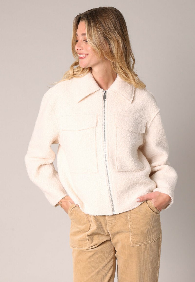 Witte, fluffy zip-up jas met twee borstzakken, kraagontwerp en textuurstof, gecombineerd met beige corduroy broek.