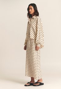 Cream polka dot blouse and matching maxi skirt, featuring black dots, lightweight fabric, relaxed fit, and long sleeves. Worn with black sandals.