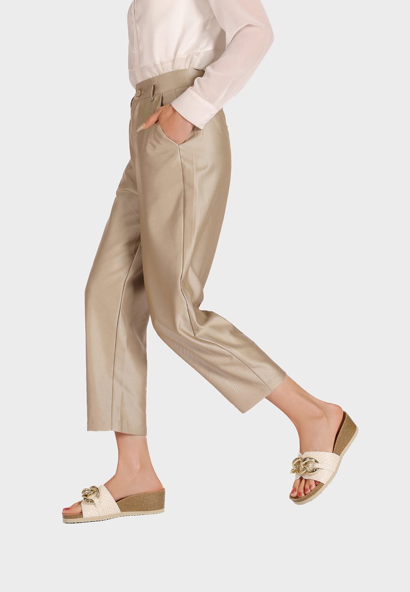 Pantaloni in satin beige con vestibilità sartoriale e tasche laterali, abbinati a sandali in crema con fibbia a scivolo caratterizzati da una texture intrecciata e inserto in oro.