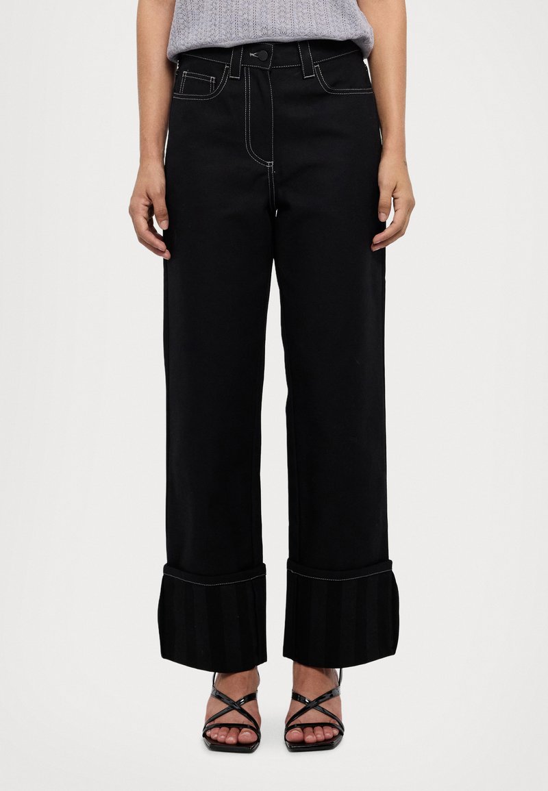 Pantaloni neri a gamba larga con cuciture bianche a contrasto, caratterizzati da un design unico con risvoltosottonato a strisce e un classico stile a cinque tasche.