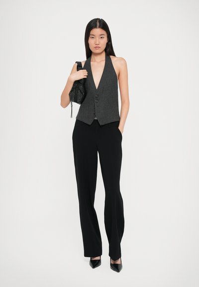 Pantalons noirs taille haute associés à un gilet dos nu gris à rayures avec un décolleté en V profond et une fermeture à trois boutons.