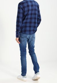 Navy and blue plaid shirt, cotton fabric, button-down collar, paired with blue jeans and white sneakers, viewed from the back.