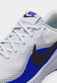 Λευκό και μπλε παπούτσι τρεξίματος Nike με μαύρο σήμα, λευκά κορδόνια και ανθεκτικό ανάγλυφο δίχτυ στο πάνω μέρος.