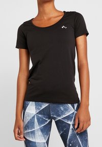 Svart t-shirt med kort ärm och rundad halslinning, med liten vit logotypdetalj på bröstet, tillverkad av ett mjukt material.