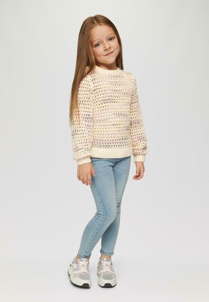 Cremefarbener Strickpullover mit mehrfarbigen Mustern, langen Ärmeln und gerippten Bündchen, kombiniert mit hellblauen Jeans und Sneakers.