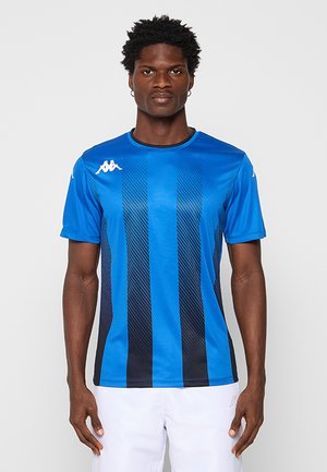 Homme faisant face à l'avant portant un maillot de sport bleu et noir à rayures verticales et un short blanc sur un fond neutre.