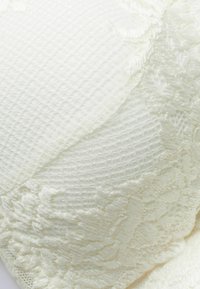 Kanten beha met een gewoven witte stof met gladde en ribbelige secties. Opvallende bloemenkant details langs de randen.
