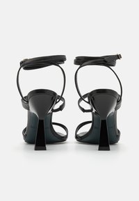 Sandales à talons hauts noires avec des sangles de cheville fines, en cuir lisse, à bout pointu et avec un talon aiguille brillant.
