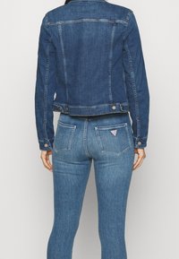 Mörkblå denimjacka med en figursydd design, knäppning med knappar och detalj på ryggen. Parat med midjebyxor i blått med bakfickor.