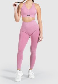 Rosa Sport-BH und hochtaillierte Leggings aus elastischem Stoff. Merkmale ein V-Ausschnitt-Design und eine strukturierte Oberfläche. Getragen mit wei�ßen Sneakers.