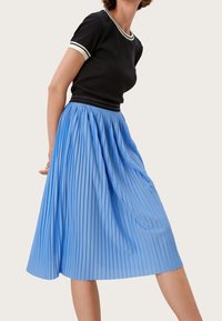 Camiseta negra de canalé con cuello y puños blancos, combinada con una falda midi plisada de color azul claro. La falda cuenta con una cinturilla elástica.