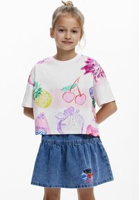Vit croppad t-shirt med färgglada frukter och blommor illustrerade, tillsammans med en jeanskjol med broderat mönster och resår i midjan.