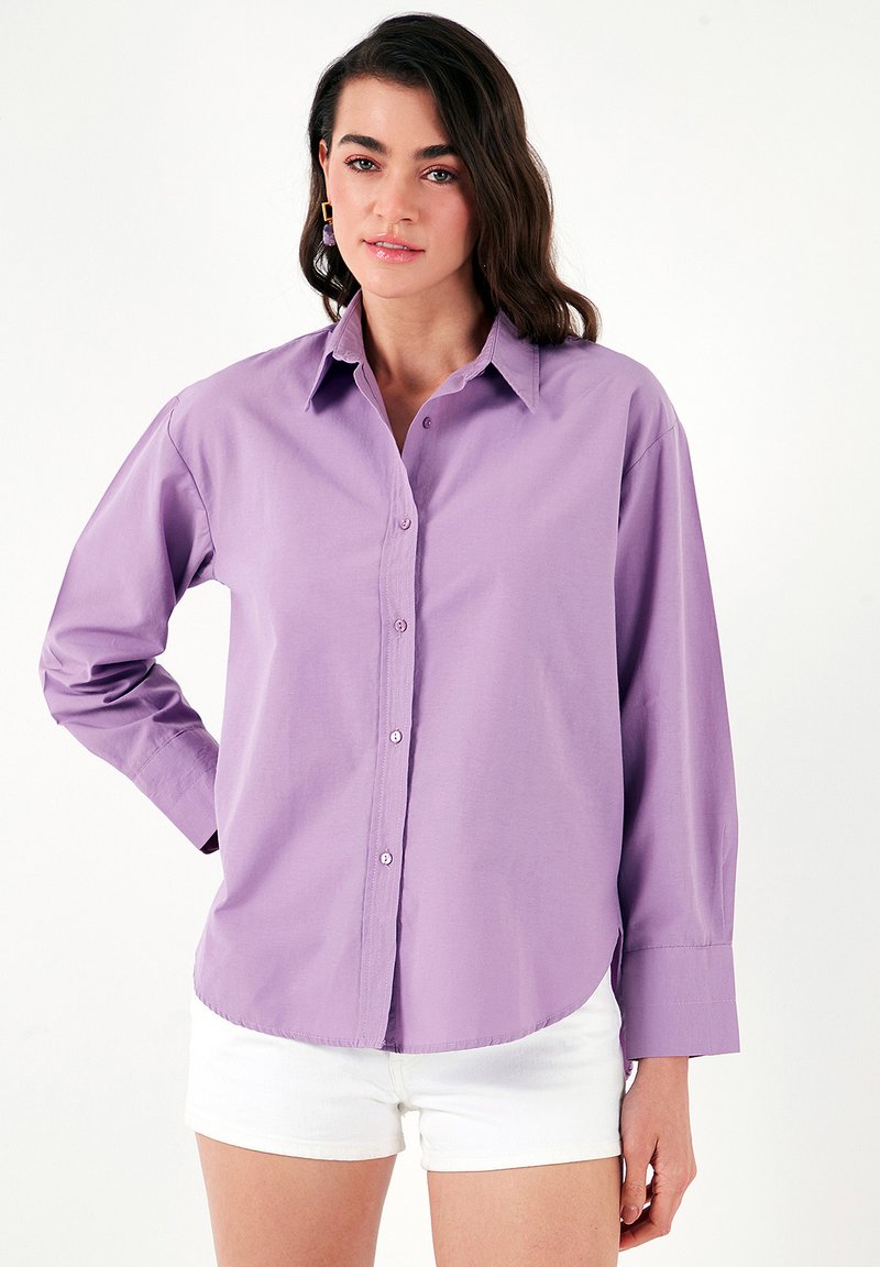Light purple button-up shirt made of cotton with long sleeves, a collar, and rounded hem; styled with white shorts.