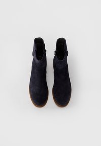 Bottines en suede bleu marine avec une texture lisse, dotées d'une fermeture éclair et d'une semelle marron contrastante. Design minimaliste, sans ornements.