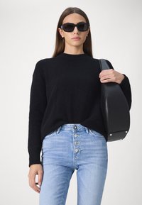 Suéter negro de pelusa con un cuello alto, jeans de mezclilla de lavado claro con una bragueta de cinco botones y un bolso negro estructurado.