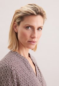 Blusa a maniche lunghe, a motivi in marrone e bianco, con scollatura a V. Tessuto morbido con stampa geometrica e una leggera texture.