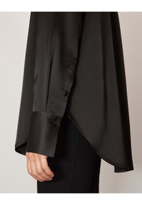 Camicia nera in satin oversized con maniche lunghe e polsini abbottonati, dotata di orlo curvo e superficie liscia. Design minimalista, senza pattern.