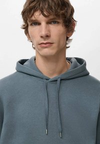 Szara bawełniana bluza z kapturem ze sznurkiem, o gładkiej fakturze i srebrnych końcówkach sznurków. Prosty, nowoczesny design bez wzorów.