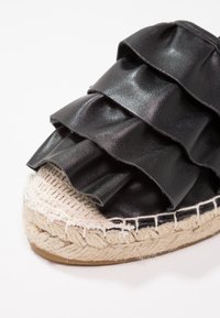 Espadrille nera con dettagli a rouches sovrapposti, suola in juta intrecciata, tomaia in materiale sintetico liscio e bordo in fibra naturale texturizzata.