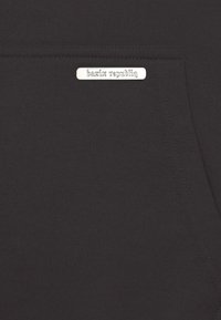 Sort sweatshirt med tekstureret stof, en frontlomme og en sølvlogo-plade med teksten "bazix republiq."