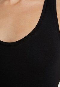 Débardeur noir avec un décolleté en rond, en coton doux et sans coutures visibles, mettant en avant un design minimaliste.