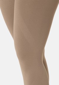 Beige tights with a smooth texture, featuring a wavy tonal pattern and ribbed detailing along the sides for added visual interest.