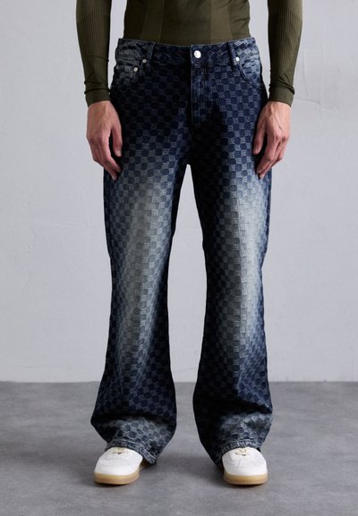 Jeans in denim blu con una stampa a scacchi, gamba larga e una finitura invecchiata. Abbinati a sneakers bianche e a un top fitted scuro.