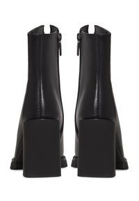 Paire de bottines en cuir noir avec talons hauts épais et fermetures éclair au dos, vues de dos sur fond blanc.