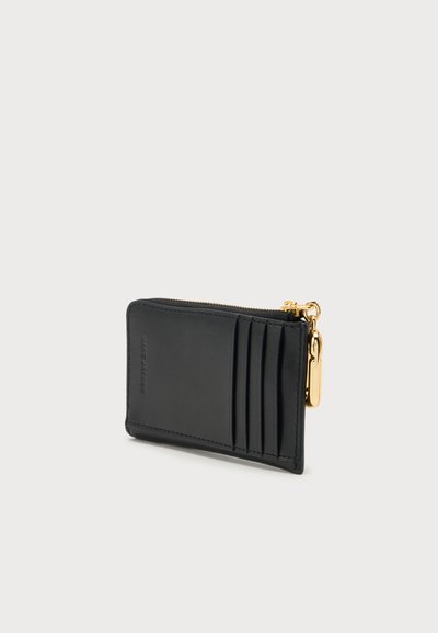 Porte-cartes en cuir noir avec quatre emplacements pour cartes et une fermeture éclair dorée en haut à droite sur un fond clair uni.