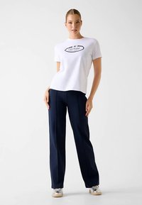 T-shirt en coton blanc avec impression de logo noir, associé à un pantalon large bleu marine et des baskets ornées d'accents argentés.