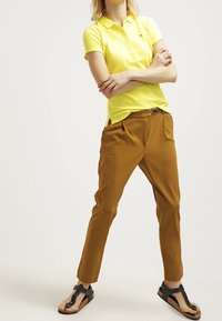 Gul polotröja med en krage, kombinerad med bruna smala byxor. Svarta sandaler med platt sula och justerbara remmar.