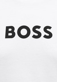 Letras mayúsculas negras en negrita que forman la palabra "BOSS" centradas sobre un fondo blanco liso, probablemente impresas en tela.