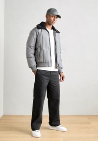 Doudoune grise avec col en polaire noir, chemise blanche, pantalon sombre et baskets blanches. Design décontracté avec une coupe ample.