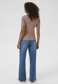Haut ajusté marron clair avec un col en dentelle et une finition scallopée, associé à un jean bleu flare taille haute et des chaussures à talons beiges.